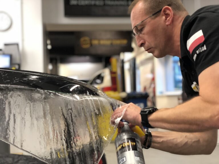 Pracownik aplikujący folię reklamową na element pojazdu